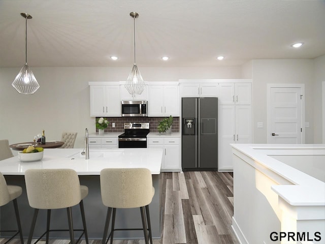 kitchen with pendant lighting, dark wood-style flooring, a kitchen breakfast bar, white cabinets, and stainless steel appliances