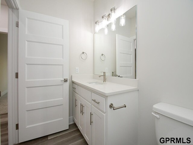 half bathroom with toilet, wood finished floors, and vanity