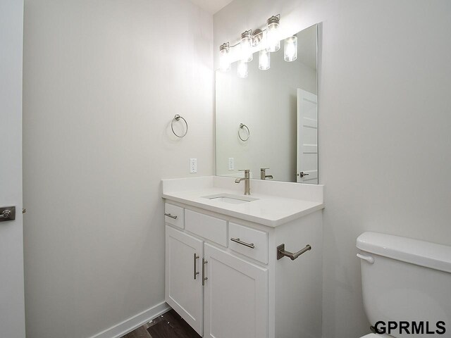half bath with vanity, wood finished floors, and toilet