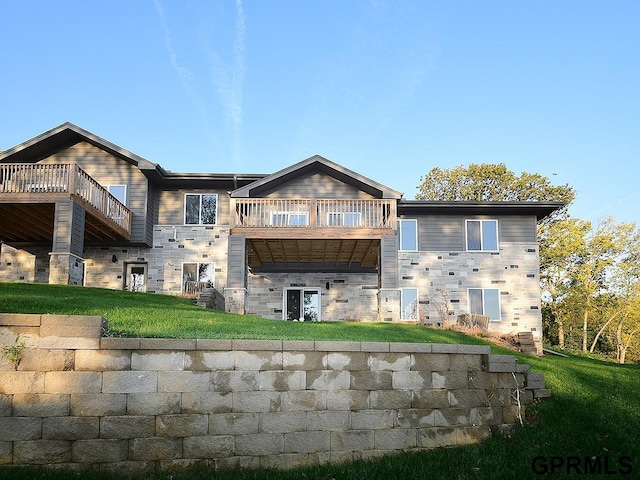 back of property with a lawn, a balcony, and stone siding