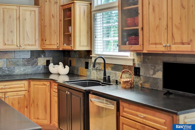 kitchen with stainless steel dishwasher, a sink, backsplash, and dark countertops