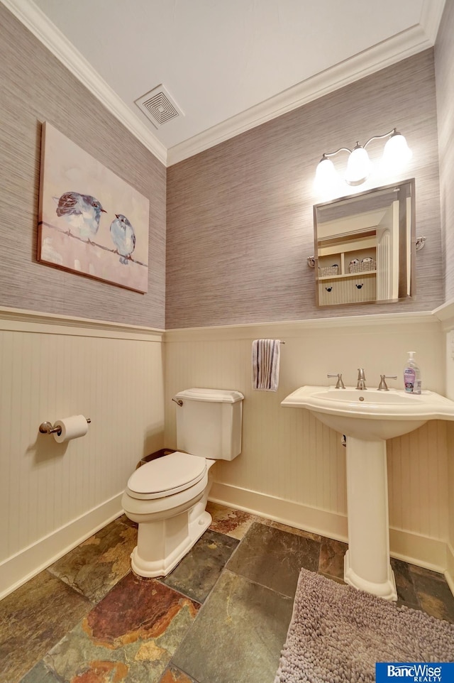 half bath featuring baseboards, stone finish flooring, toilet, a wainscoted wall, and ornamental molding