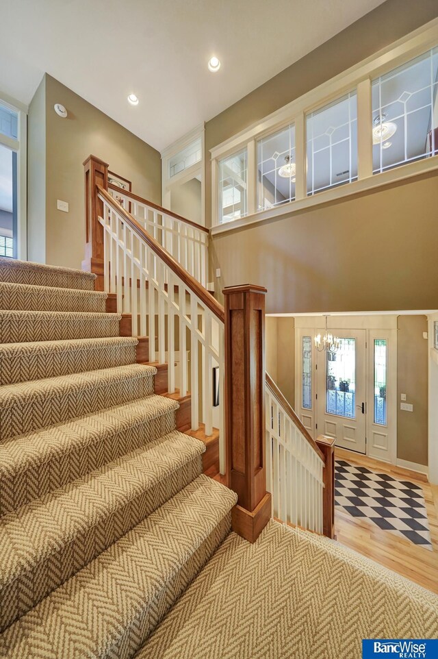 staircase featuring a chandelier, wood finished floors, recessed lighting, and a high ceiling