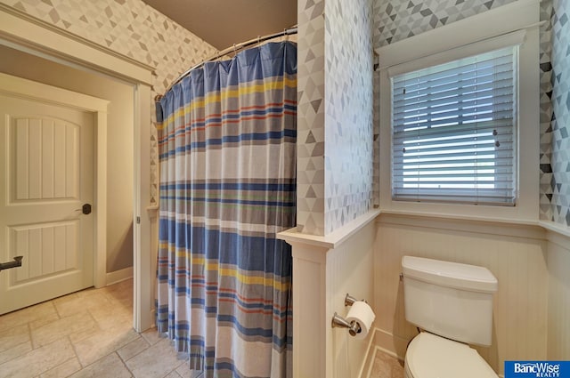 full bath featuring stone tile floors, wallpapered walls, toilet, and a shower with shower curtain