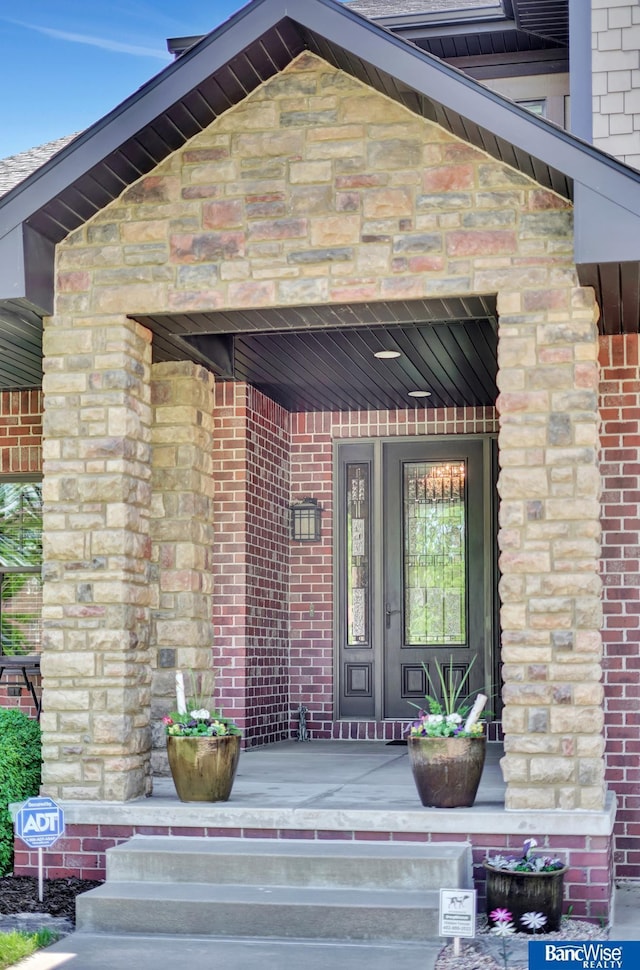 doorway to property featuring a porch, stone siding, and brick siding
