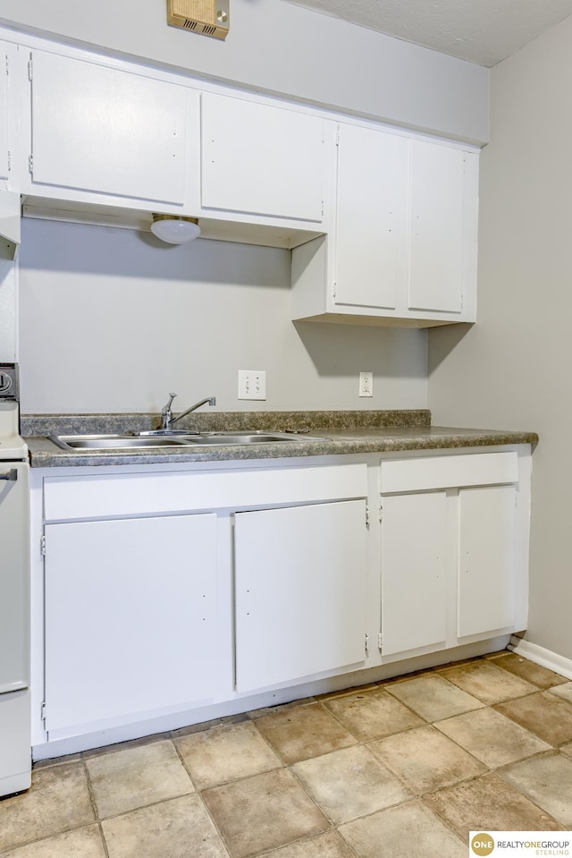 kitchen with stone finish floor, visible vents, white range with electric cooktop, a sink, and white cabinets