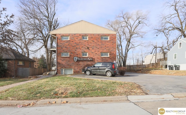 exterior space featuring fence, central AC, brick siding, a lawn, and driveway