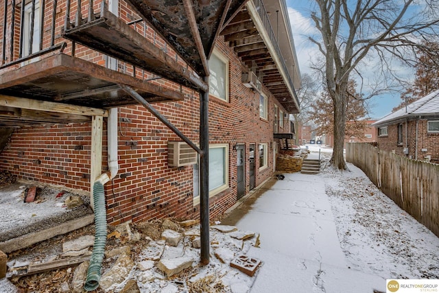 view of snowy exterior featuring fence, an AC wall unit, and brick siding