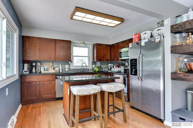 kitchen featuring a kitchen island, light wood-type flooring, a sink, a breakfast bar, and stainless steel appliances