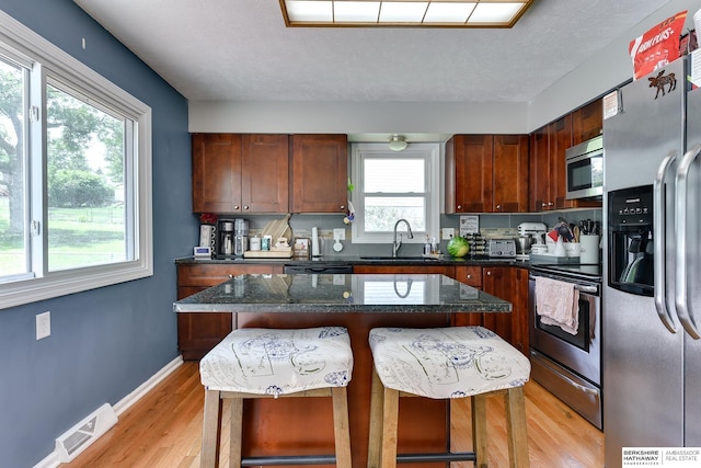 kitchen with visible vents, a sink, a breakfast bar, stainless steel appliances, and light wood-style flooring