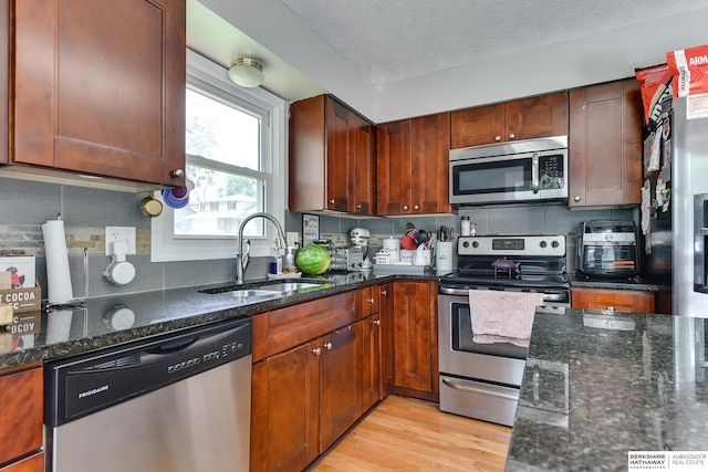 kitchen with tasteful backsplash, light wood-type flooring, a sink, dark stone countertops, and stainless steel appliances