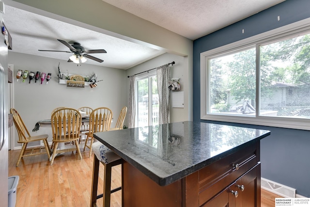 kitchen with light wood finished floors, a breakfast bar area, a textured ceiling, a ceiling fan, and visible vents