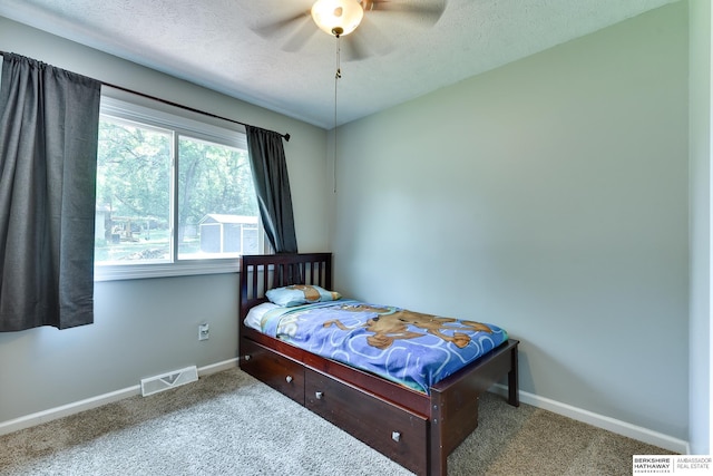 carpeted bedroom with a textured ceiling, baseboards, visible vents, and a ceiling fan