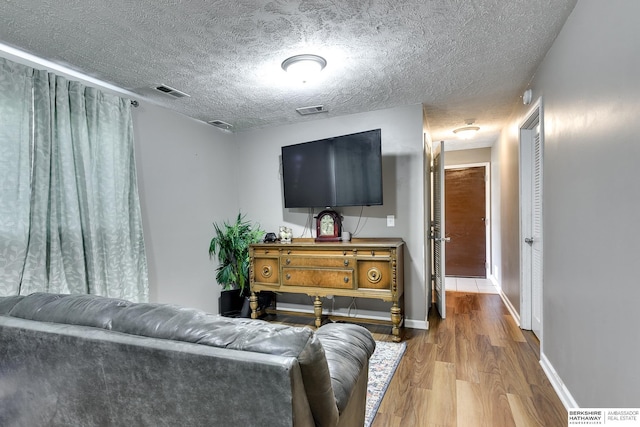 living area with baseboards, a textured ceiling, visible vents, and wood finished floors