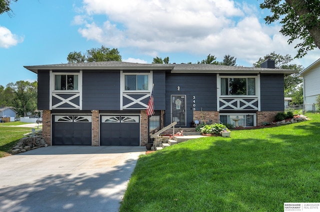 bi-level home featuring a garage, a front lawn, a chimney, brick siding, and driveway