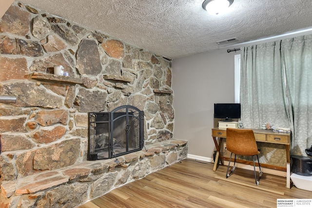 home office with a textured ceiling, visible vents, a fireplace, wood finished floors, and baseboards
