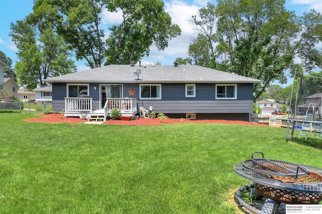 back of property with a wooden deck, fence, a trampoline, and an outdoor fire pit