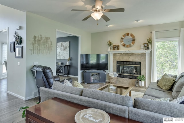 living room with baseboards, ceiling fan, a fireplace, and wood finished floors