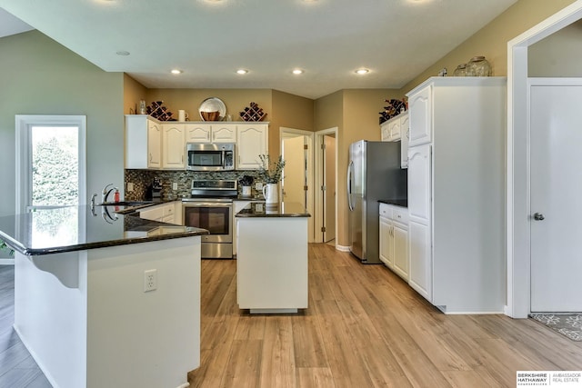 kitchen featuring tasteful backsplash, white cabinets, light wood finished floors, a peninsula, and stainless steel appliances