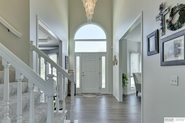 foyer entrance featuring an inviting chandelier, a towering ceiling, wood finished floors, baseboards, and stairway