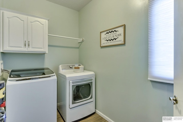 clothes washing area featuring cabinet space, washing machine and dryer, and light wood finished floors