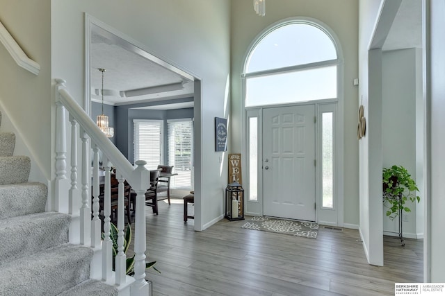 foyer with a towering ceiling, wood finished floors, baseboards, an inviting chandelier, and stairs