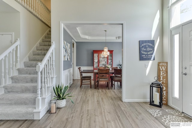 entrance foyer featuring wainscoting, wood finished floors, an inviting chandelier, a tray ceiling, and stairs
