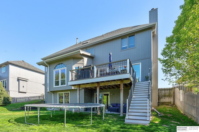 back of house with a wooden deck, a fenced backyard, a trampoline, a yard, and stairway