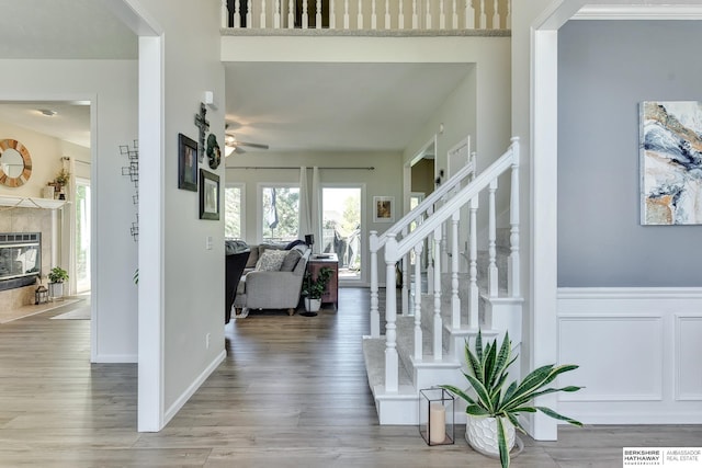 entrance foyer with wood finished floors, a fireplace, ceiling fan, stairway, and a wainscoted wall