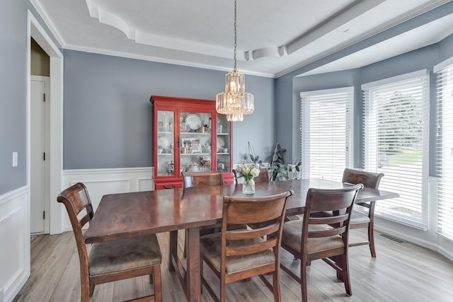 dining area featuring visible vents, light wood-style floors, a wainscoted wall, a tray ceiling, and a chandelier