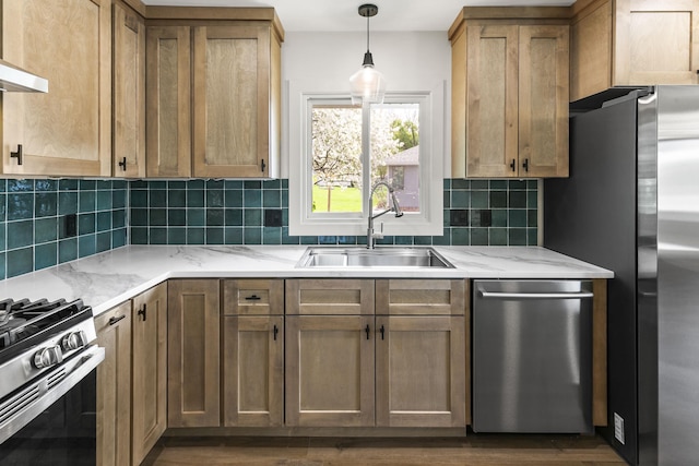 kitchen featuring light stone countertops, hanging light fixtures, a sink, stainless steel appliances, and backsplash