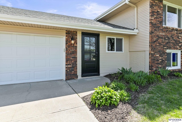 view of exterior entry with brick siding, a shingled roof, a garage, and concrete driveway