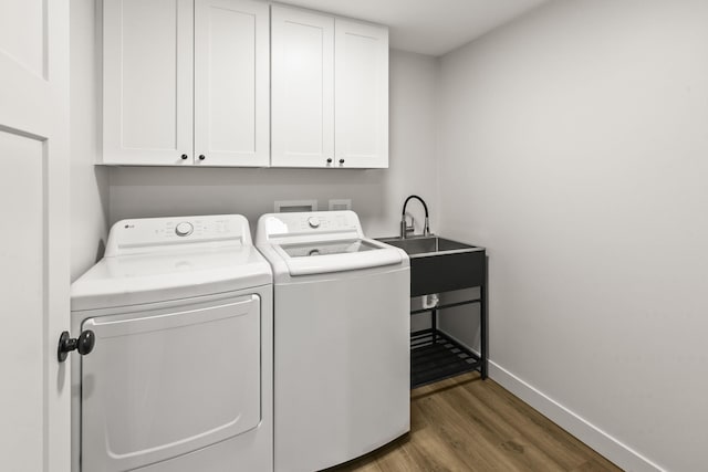 washroom featuring washing machine and clothes dryer, cabinet space, a sink, baseboards, and wood finished floors