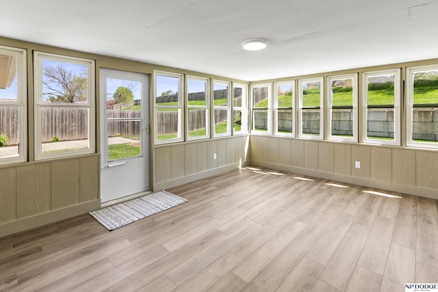 unfurnished sunroom featuring a healthy amount of sunlight, a deck, baseboards, and wood finished floors