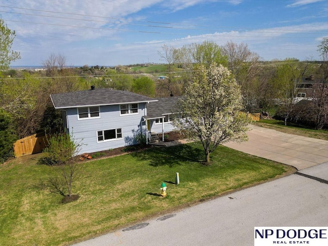 view of front of property featuring concrete driveway, fence, a shingled roof, and a front yard