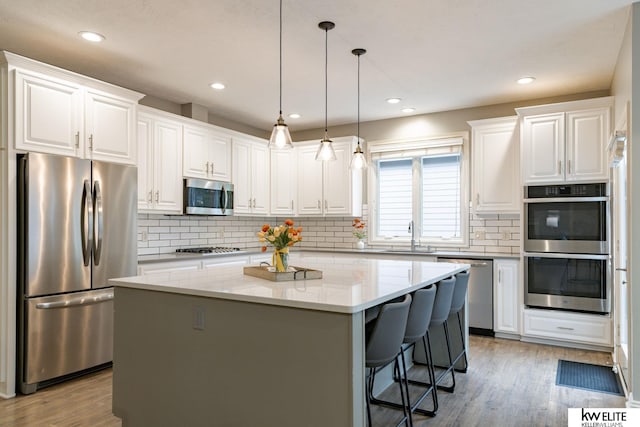 kitchen featuring a center island, white cabinetry, a sink, light wood finished floors, and stainless steel appliances