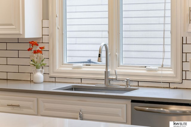details featuring a sink, stainless steel dishwasher, backsplash, and white cabinetry