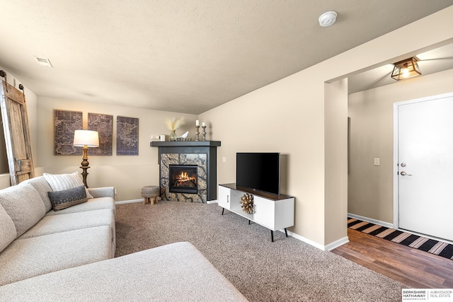 carpeted living room featuring baseboards, visible vents, a barn door, and a fireplace