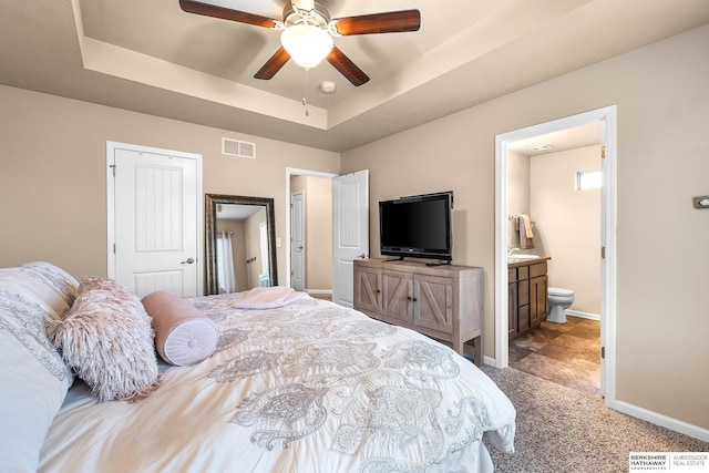 carpeted bedroom with visible vents, connected bathroom, a raised ceiling, and baseboards