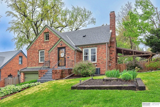 tudor home with fence, an attached garage, a front lawn, brick siding, and a chimney