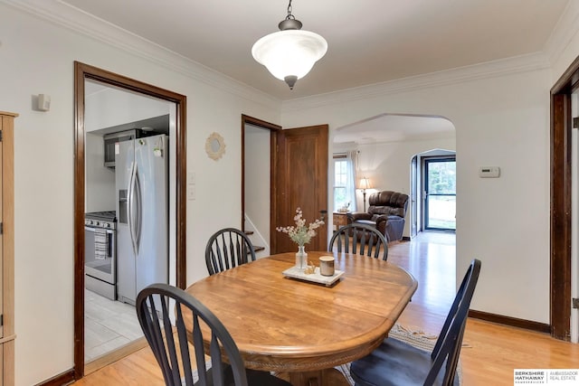 dining area featuring crown molding, arched walkways, baseboards, and light wood-style flooring