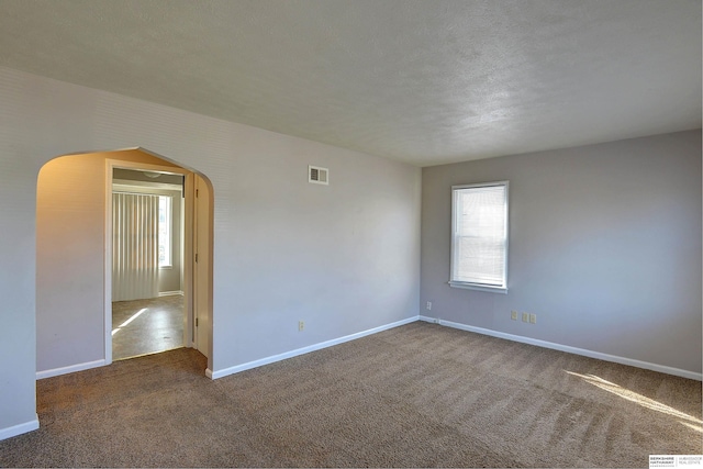 unfurnished room with arched walkways, baseboards, carpet flooring, and visible vents