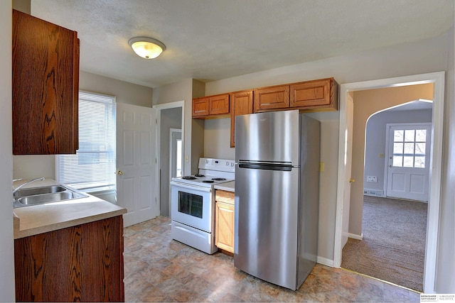 kitchen with arched walkways, a sink, light countertops, freestanding refrigerator, and white range with electric stovetop