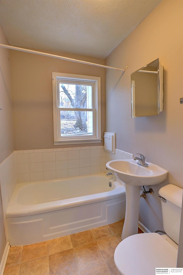 full bathroom with a bathing tub, toilet, a textured ceiling, and tile patterned flooring
