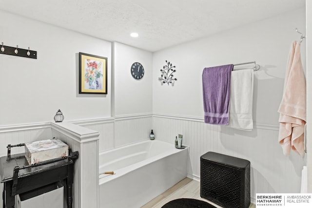 full bath with a garden tub, a textured ceiling, a decorative wall, and a wainscoted wall