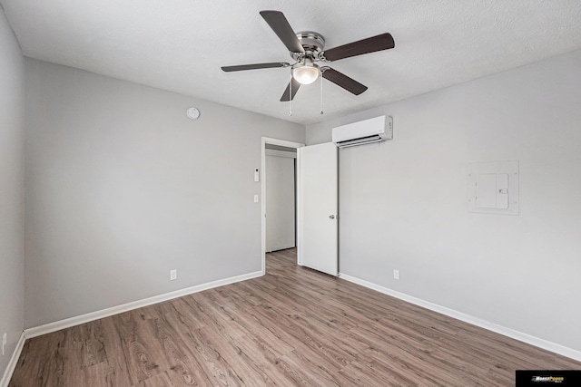 unfurnished bedroom featuring baseboards, ceiling fan, a wall mounted AC, and wood finished floors
