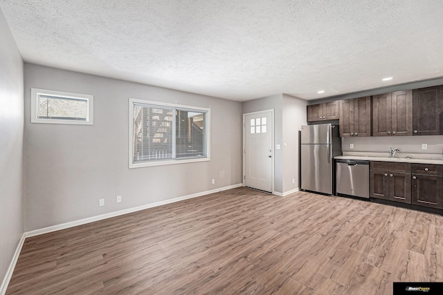 kitchen featuring dark brown cabinetry, light wood-type flooring, light countertops, a textured ceiling, and appliances with stainless steel finishes