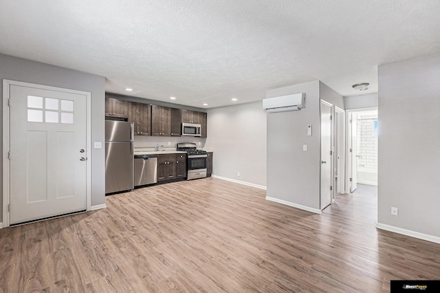 kitchen featuring appliances with stainless steel finishes, a wall mounted AC, dark brown cabinets, light countertops, and baseboards