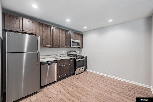 kitchen featuring dark brown cabinets, baseboards, light wood-type flooring, a sink, and appliances with stainless steel finishes