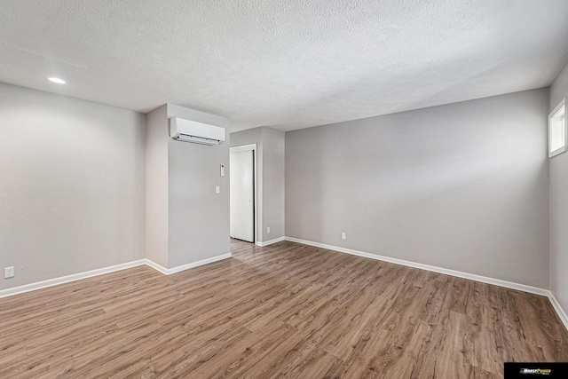 spare room with a textured ceiling, a wall unit AC, baseboards, and light wood-style floors